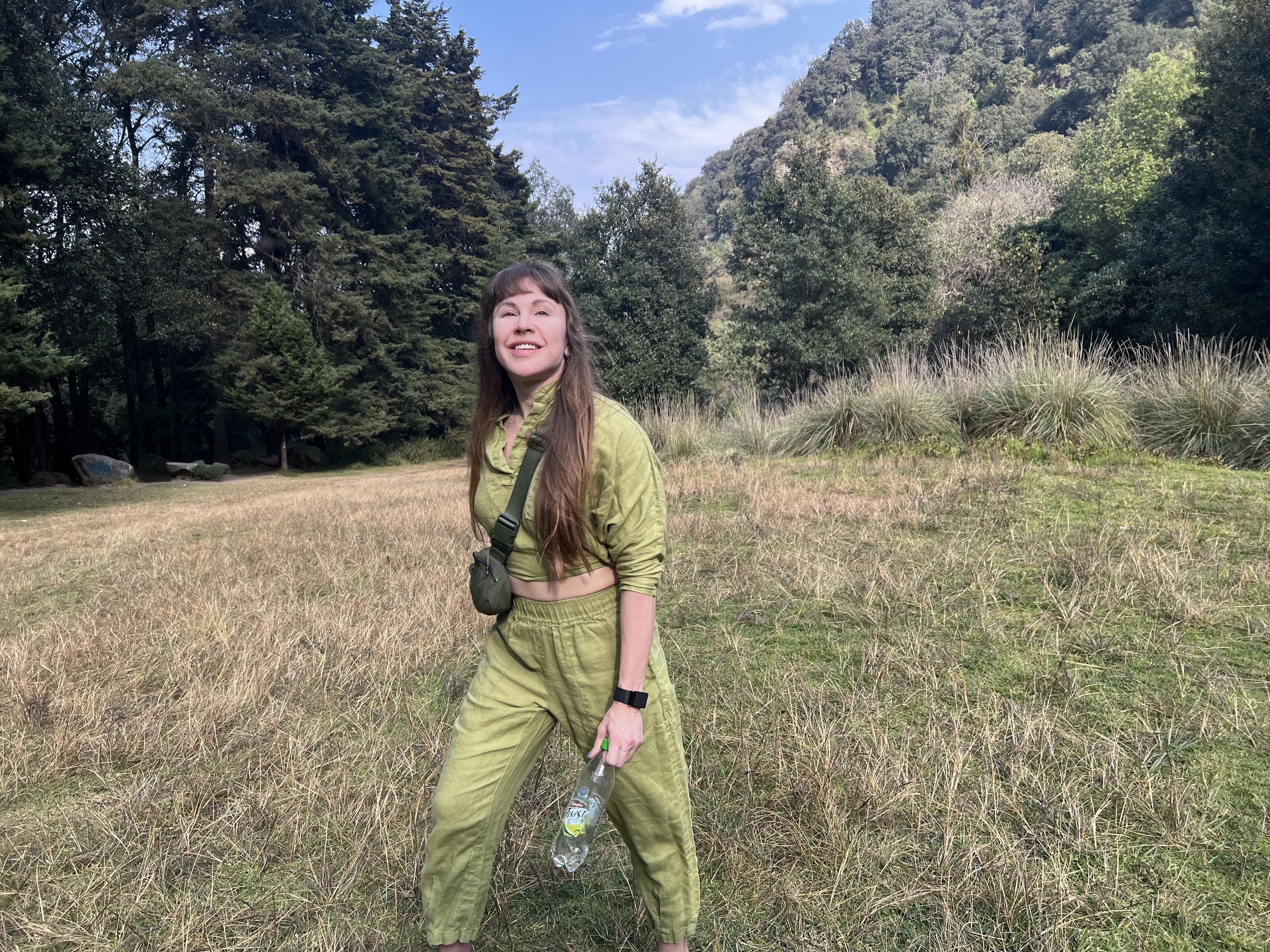 Mars smiling in an olive outfit in a sunlit Colombian mountain valley